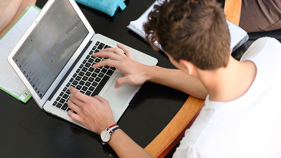 Ein Student sitzt an einem Tisch und schreibt auf seinem Laptop.