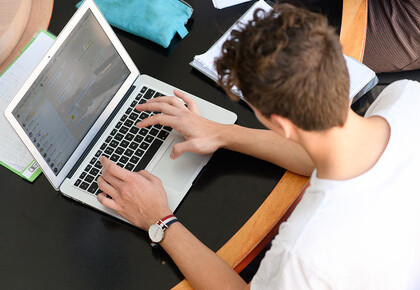 Ein Student sitzt an einem Tisch und schreibt auf seinem Laptop.