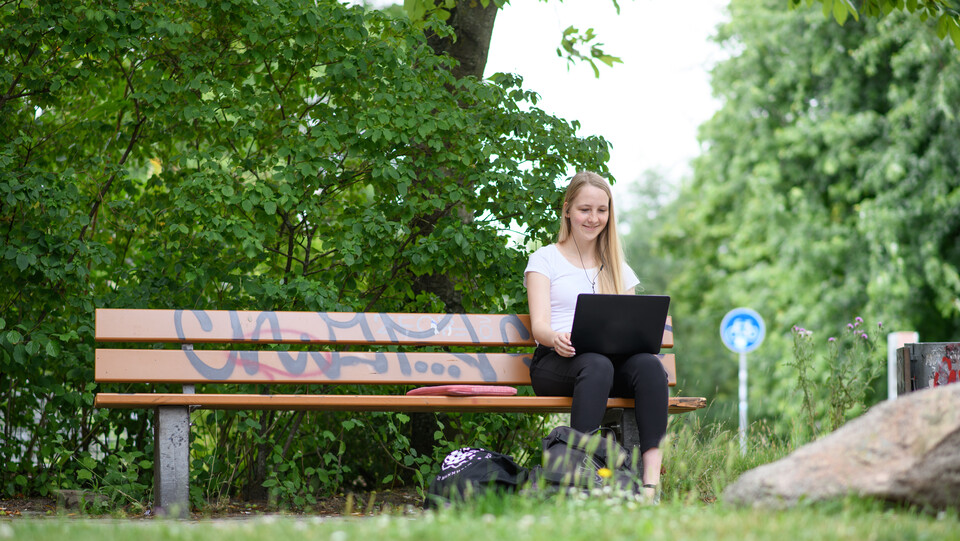 Studentin mit Laptop auf einer Parkbank