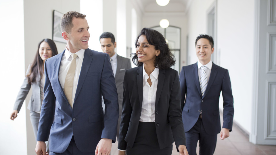Personen in Business Kleidung laufen den Flur entlang