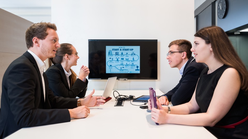 Studierende sitzen um Tisch mit Bildschirm