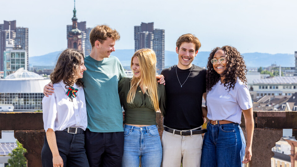 Fünf Studierende stehen auf dem Dach des Barockschlosses für ein Gruppenfoto. Im Hintergrund ist die Stadt Mannheim zu sehen.