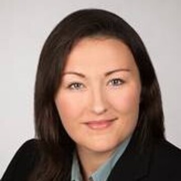 Eva Koenig hat schwarze lange Haare und trägt einen schwarzen Blazer und eine graue Bluse