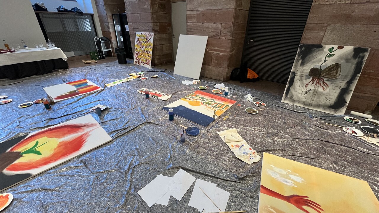 Gemalte Bilder und Malutensilien liegen auf dem Boden verteilt.
