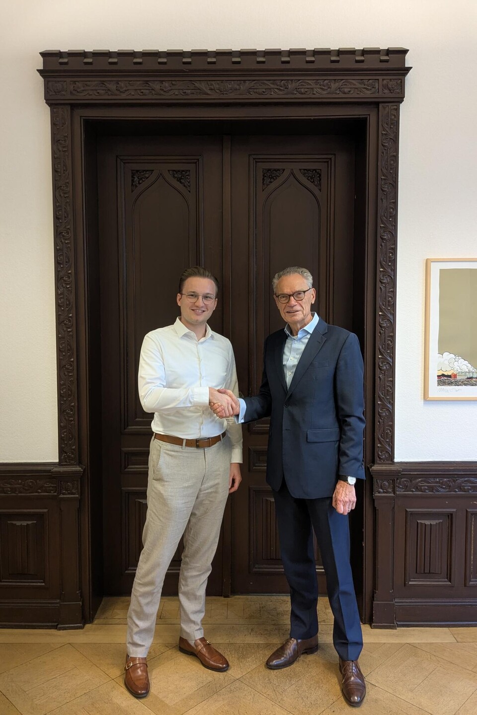 Till Muenster und Joachim Lutz stehen vor einer dunkelbraunen Tür und schütteln sich die Hand