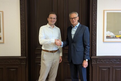 Till Muenster und Joachim Lutz stehen vor einer dunkelbraunen Tür und schütteln sich die Hand