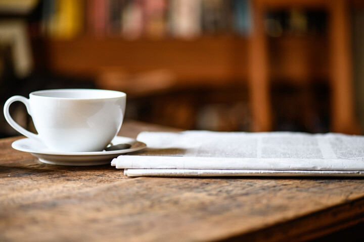 Eine Zeitung und eine Kaffeetasse stehen auf einem Holztisch.