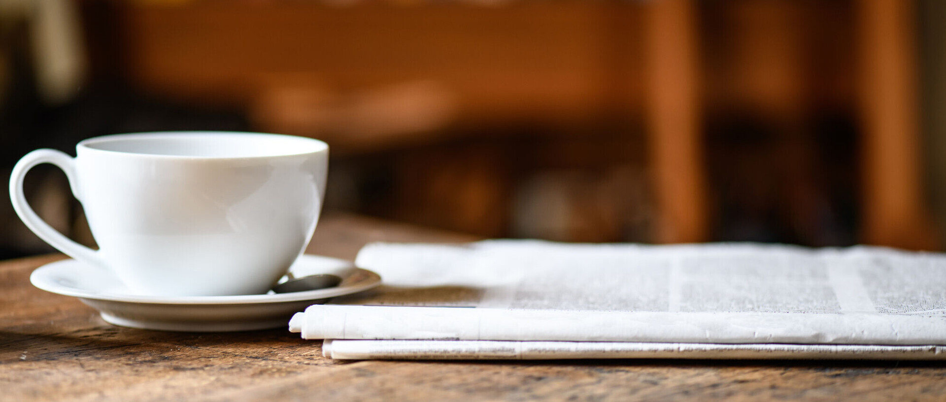 Eine Zeitung und eine Kaffeetasse stehen auf einem Holztisch.
