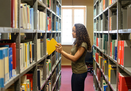 Eine Studentin zieht ein gelbes Buch aus einem Bücherregal in der Bibliothek.