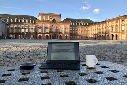 Laptop auf Bank mit Kaffeetasse im Ehrenhof des Schlosses