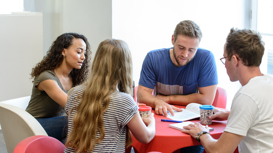 Vier Studierende sitzen an einem runden Tisch und lernen gemeinsam.