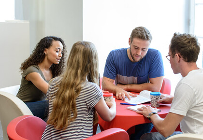 Vier Studierende sitzen an einem runden Tisch und lernen gemeinsam.