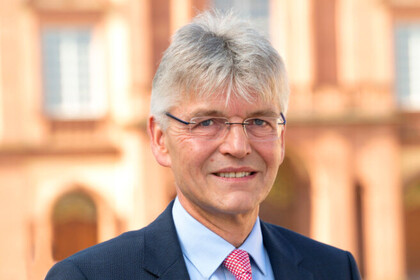 Christoph Spengel hat kurze graue Haare. Er trägt eine schmale Brille, ein hellblaues Hemd, eine rote Krawatte und ein schwarzes Jackett.