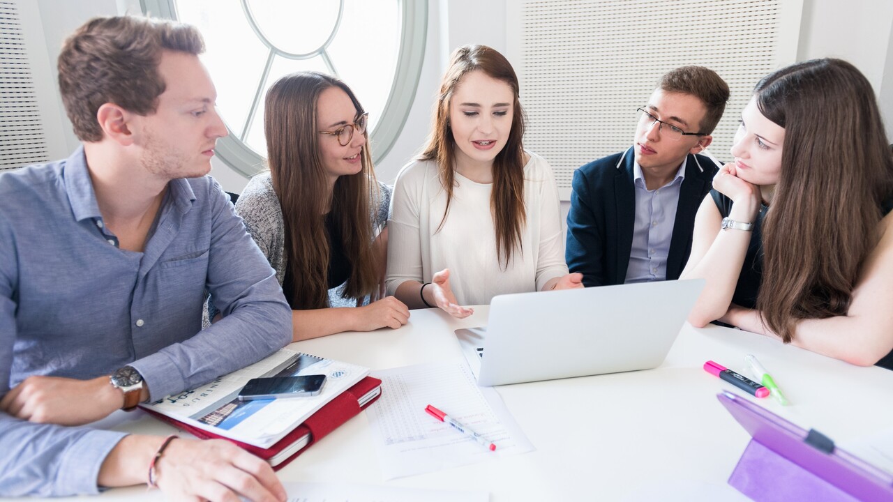 Students with laptops sit around a table