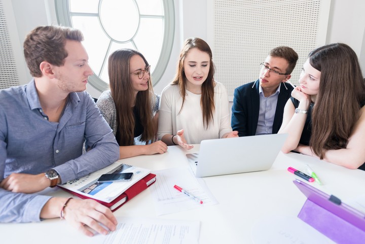 Studierende mit Laptops sitzen um einen Tisch