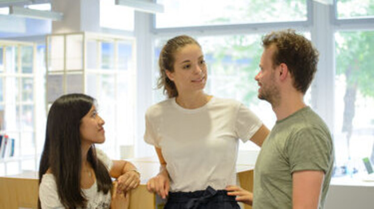 Three people are standing in front of a glass wall talking.