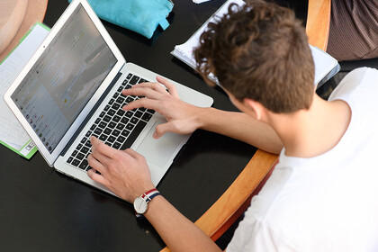 Ein Student sitzt an einem Tisch und schreibt auf seinem Laptop.