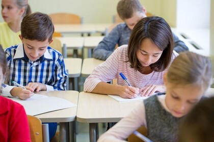 Schüler*innen sitzen nebeneinander an Tischen und schreiben auf ein Blatt Papier.